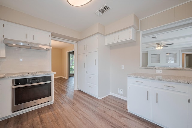 1316 Courtney St, Richmond, TX 77469 - kitchen featuring stainless steel oven, under cabinet range hood, tasteful backsplash, light wood-style flooring, and white cabinetry