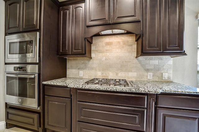 4011 Teramo Ln, Katy, TX 77493 - kitchen with stainless steel appliances, dark brown cabinetry, decorative backsplash, and light stone counters