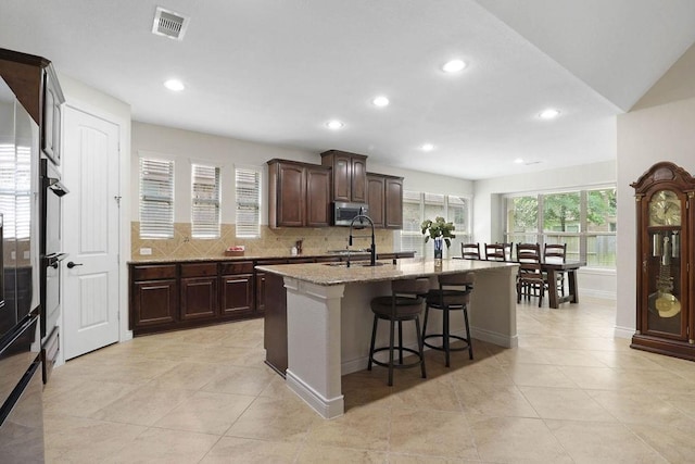 266 Overland Trce, Montgomery, TX 77316 - kitchen featuring stainless steel microwave, a kitchen bar, tasteful backsplash, light tile patterned floors, and an island with sink