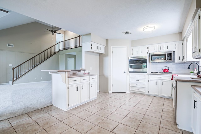 1313 Mcdonald St, Deer Park, TX 77536 - kitchen with stainless steel appliances, light tile patterned floors, white cabinetry, ceiling fan, and decorative backsplash