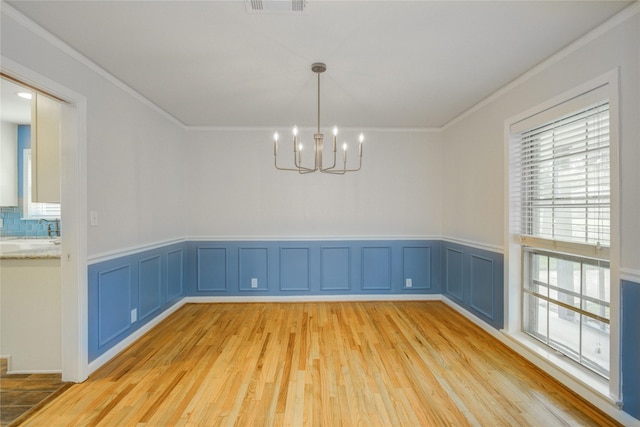 5007 Redstart St, Houston, TX 77035 - unfurnished dining area featuring a chandelier, ornamental molding, light wood-style floors, a wainscoted wall, and a decorative wall