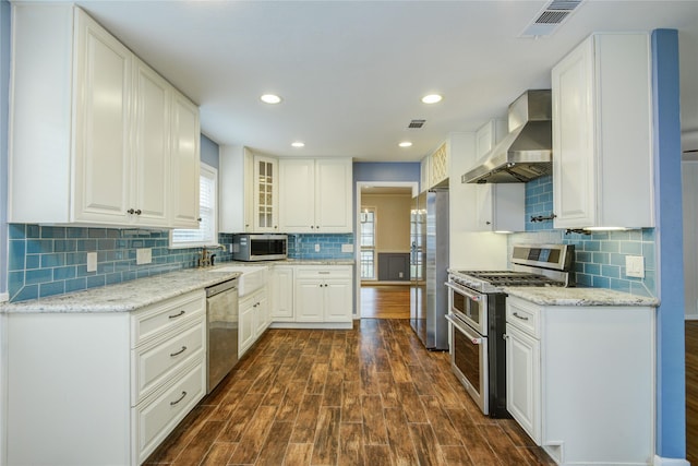 5007 Redstart St, Houston, TX 77035 - kitchen featuring appliances with stainless steel finishes, wall chimney exhaust hood, dark wood-style flooring, backsplash, and white cabinets