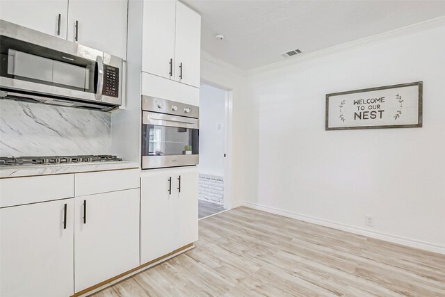 7650 US Highway 69 S, Woodville, TX 75979 - kitchen with appliances with stainless steel finishes, crown molding, light wood-style floors, white cabinetry, and decorative backsplash