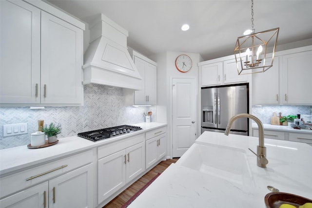 2331 Hagerman Rd, Conroe, TX 77384 - kitchen featuring appliances with stainless steel finishes, custom exhaust hood, a chandelier, white cabinetry, and backsplash