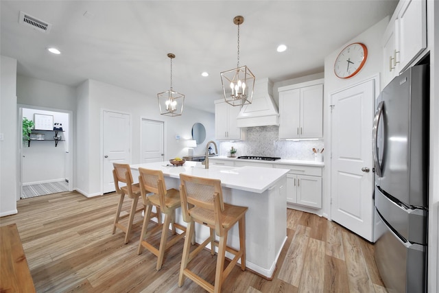 2331 Hagerman Rd, Conroe, TX 77384 - kitchen featuring freestanding refrigerator, custom range hood, black gas stovetop, light wood-style floors, and decorative backsplash