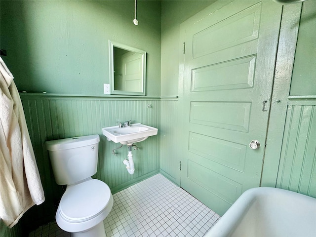 1317 Church St, Galveston, TX 77550 - bathroom with tile patterned floors, wainscoting, toilet, a soaking tub, and a sink