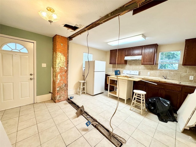 1317 Church St, Galveston, TX 77550 - kitchen featuring freestanding refrigerator, under cabinet range hood, light tile patterned flooring, and tasteful backsplash