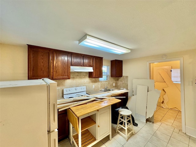 1317 Church St, Galveston, TX 77550 - kitchen featuring freestanding refrigerator, under cabinet range hood, wooden counters, light tile patterned floors, and tasteful backsplash