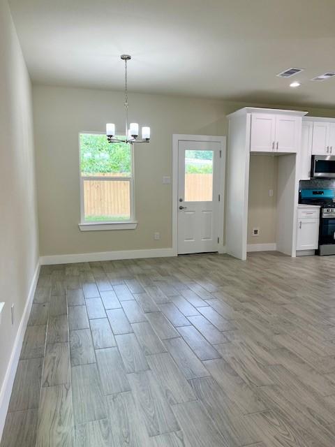 10516 Exeter St, Houston, TX 77093 - kitchen featuring appliances with stainless steel finishes, a chandelier, white cabinetry, light wood-style floors, and decorative light fixtures