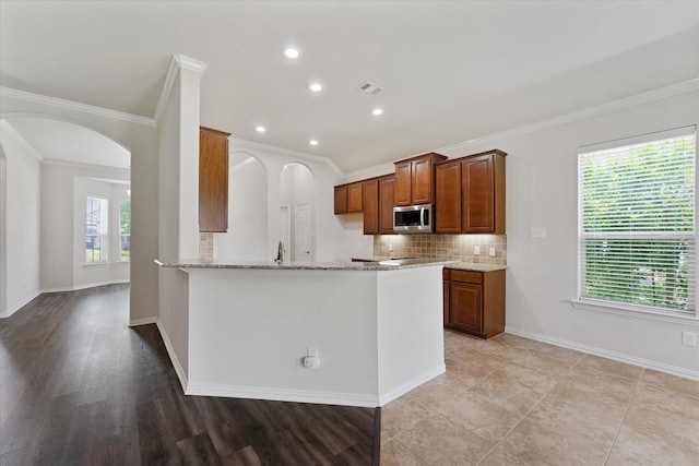 25303 Hawthorne Blossom Dr, Spring, TX 77389 - kitchen with stainless steel microwave, ornamental molding, arched walkways, light stone countertops, and backsplash