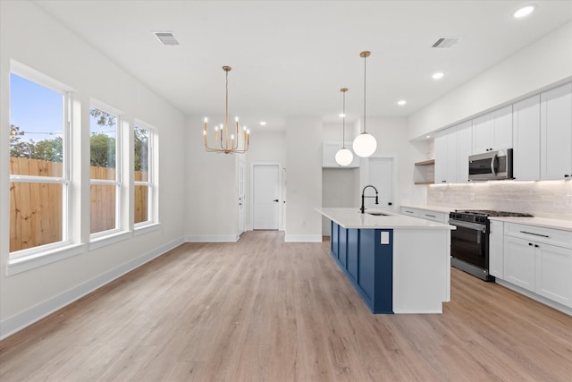 5306 San Juan St, Houston, TX 77020 - kitchen featuring range with gas cooktop, stainless steel microwave, tasteful backsplash, white cabinets, and light wood-style floors