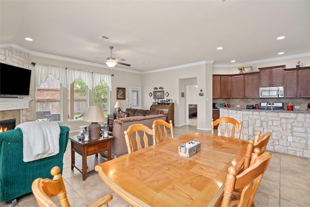207 Lockridge Hill Ln, Richmond, TX 77469 - dining space featuring ceiling fan, a warm lit fireplace, light tile patterned floors, recessed lighting, and crown molding