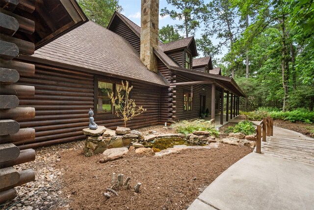 19314 Indigo Lake Dr, Magnolia, TX 77355 - view of side of home with log exterior, a shingled roof, a patio, and a chimney