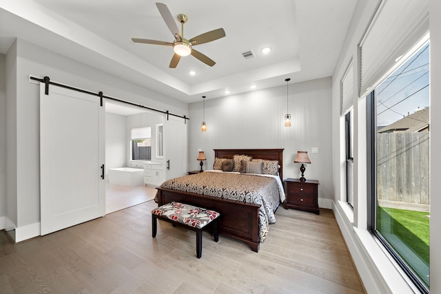 1610 Woodcrest Dr, Houston, TX 77018 - bedroom with a barn door, light wood finished floors, a tray ceiling, recessed lighting, and connected bathroom