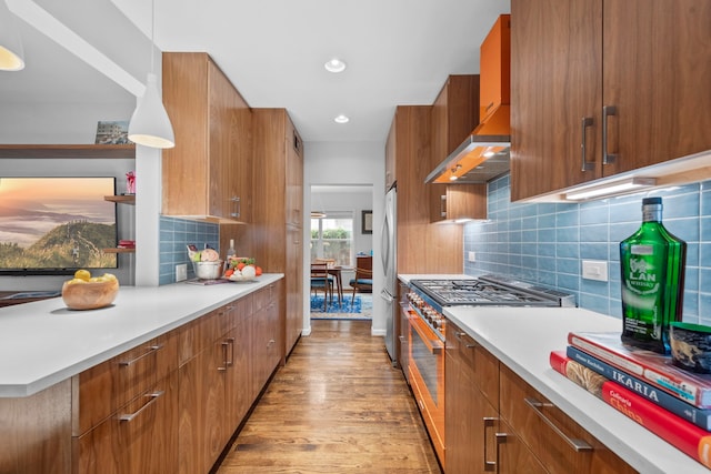 2101 Banks St, Houston, TX 77098 - kitchen featuring stainless steel appliances, wall chimney range hood, brown cabinets, light wood-style flooring, and light countertops
