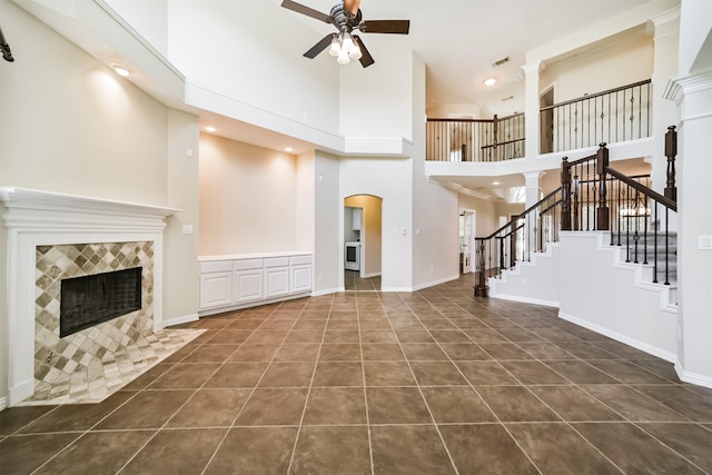 7319 Fair Meadow Ln, Katy, TX 77494 - unfurnished living room with ceiling fan, a towering ceiling, a tiled fireplace, stairway, and dark tile patterned floors