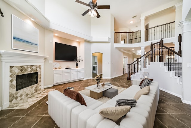 7319 Fair Meadow Ln, Katy, TX 77494 - living room with dark tile patterned flooring, a ceiling fan, a tiled fireplace, a towering ceiling, and stairs