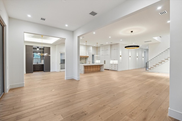 3755 Rice Blvd, Houston, TX 77005 - unfurnished living room featuring light wood-type flooring, baseboards, recessed lighting, stairs, and a sink