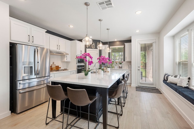 221 Sky Top Dr, Montgomery, TX 77316 - kitchen with appliances with stainless steel finishes, under cabinet range hood, light countertops, a kitchen breakfast bar, and light wood-style flooring