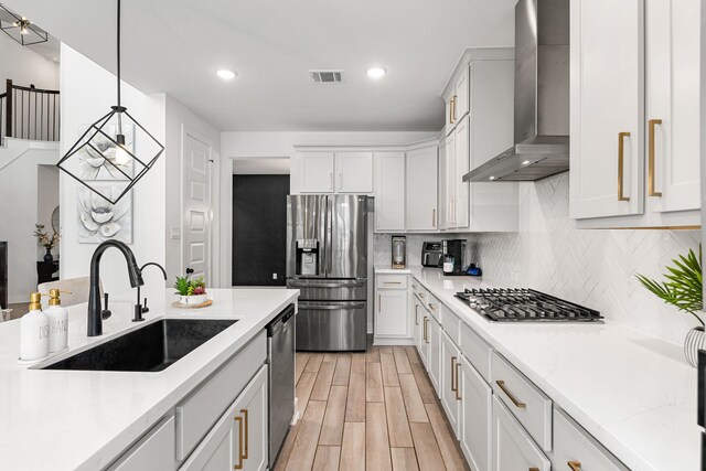 31207 Hastings Creek Ln, Fulshear, TX 77441 - kitchen featuring stainless steel appliances, a sink, wall chimney exhaust hood, light wood finished floors, and decorative backsplash
