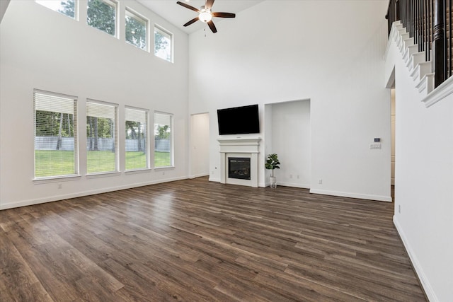 40805 Iver Ln, Magnolia, TX 77354 - unfurnished living room with ceiling fan, a towering ceiling, dark wood-type flooring, a glass covered fireplace, and baseboards