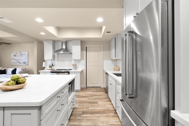 137 Litchfield Ln, Houston, TX 77024 - kitchen with stainless steel appliances, wall chimney exhaust hood, a tray ceiling, light wood-type flooring, and recessed lighting
