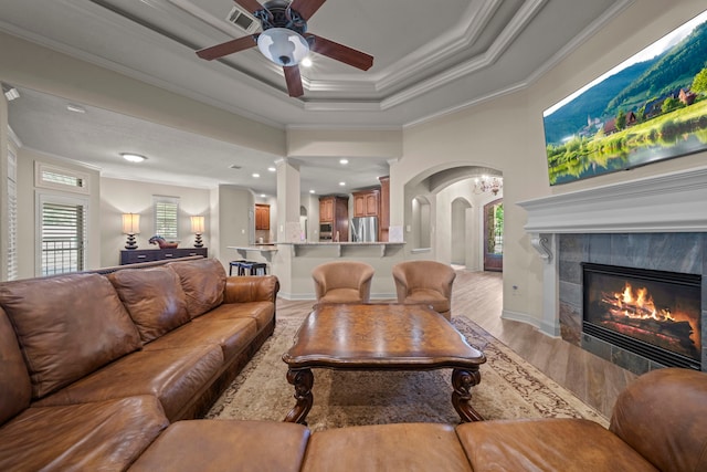 261 Ridge Lake Dr, Montgomery, TX 77316 - living area featuring crown molding, light wood finished floors, a tile fireplace, a ceiling fan, and arched walkways