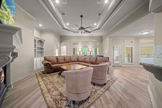 261 Ridge Lake Dr, Montgomery, TX 77316 - living area with a tray ceiling, light wood-style flooring, crown molding, a lit fireplace, and a ceiling fan