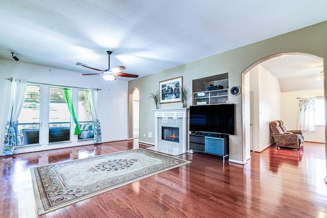 2207 Desert Vine Ct, Sugar Land, TX 77498 - living room featuring a ceiling fan, arched walkways, a tiled fireplace, wood finished floors, and baseboards