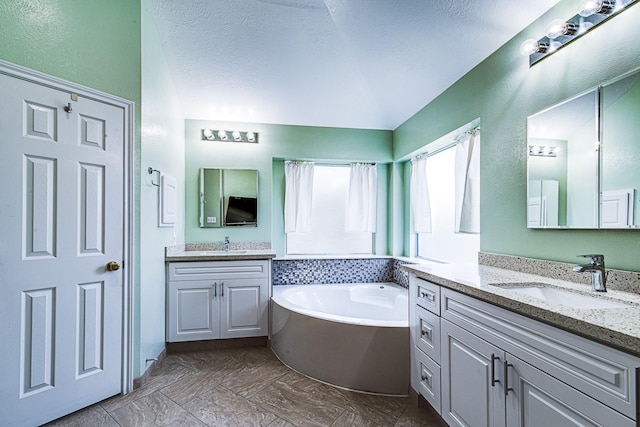 2207 Desert Vine Ct, Sugar Land, TX 77498 - bathroom featuring two vanities, a garden tub, vaulted ceiling, and a textured ceiling