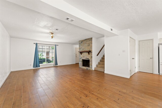14721 Perthshire Rd, Houston, TX 77079 - unfurnished living room with a textured ceiling, a large fireplace, light wood-style flooring, baseboards, and stairway