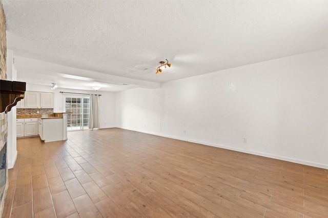 14721 Perthshire Rd, Houston, TX 77079 - unfurnished living room featuring light wood-style floors, baseboards, a textured ceiling, and a fireplace