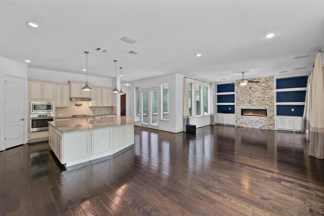 211 Twilight Toast Dr, Conroe, TX 77304 - kitchen featuring cream cabinets, stainless steel microwave, dark wood-style floors, open floor plan, and a stone fireplace