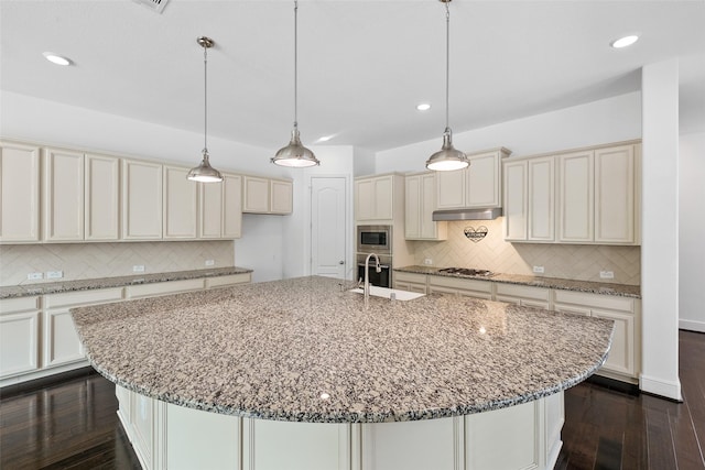 211 Twilight Toast Dr, Conroe, TX 77304 - kitchen featuring stainless steel appliances, under cabinet range hood, cream cabinetry, a sink, and decorative backsplash
