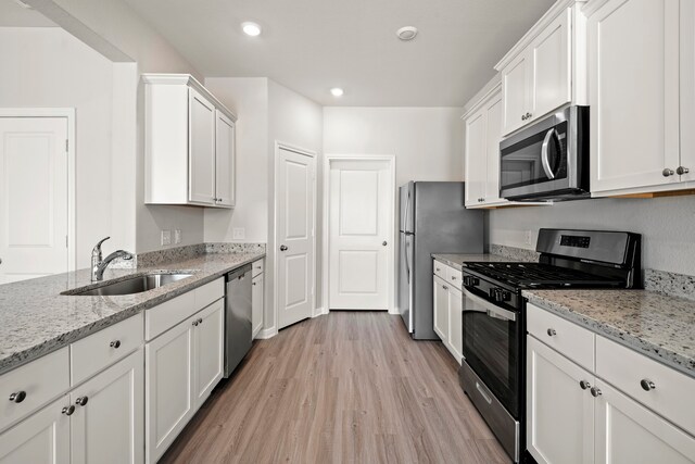 15695 Honey Cove Dr, Conroe, TX 77303 - kitchen with stainless steel appliances, a sink, light wood-style flooring, white cabinetry, and light stone counters