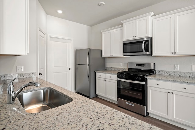 15695 Honey Cove Dr, Conroe, TX 77303 - kitchen with stainless steel appliances, a sink, white cabinets, dark wood-type flooring, and light stone counters
