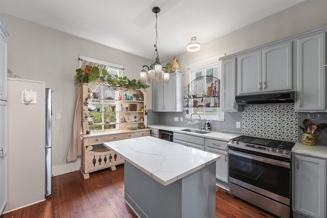 811 18th St, Galveston, TX 77550 - kitchen featuring stainless steel gas stove, under cabinet range hood, decorative backsplash, dark wood-style floors, and a chandelier