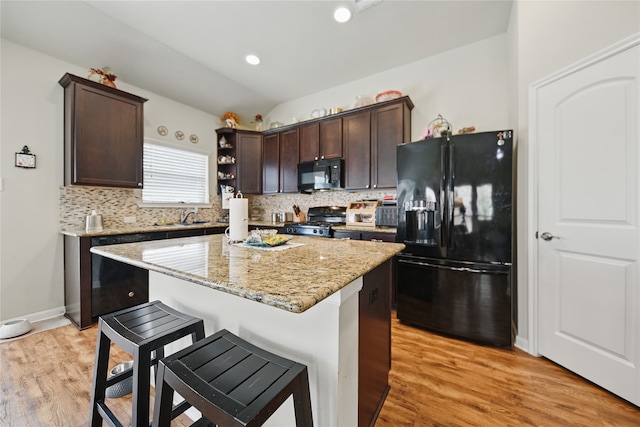 2209 Parker Ct, Brenham, TX 77833 - kitchen with black appliances, dark brown cabinetry, backsplash, a breakfast bar area, and light wood-style flooring