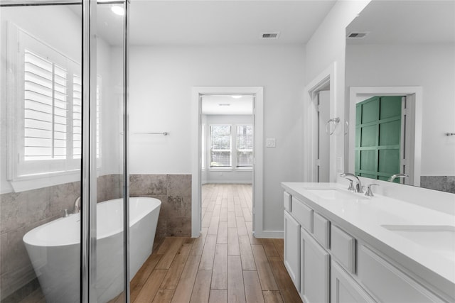 439 Flowering Lotus Ct, Willis, TX 77318 - full bathroom featuring tile walls, double vanity, a freestanding tub, wood finished floors, and a wainscoted wall