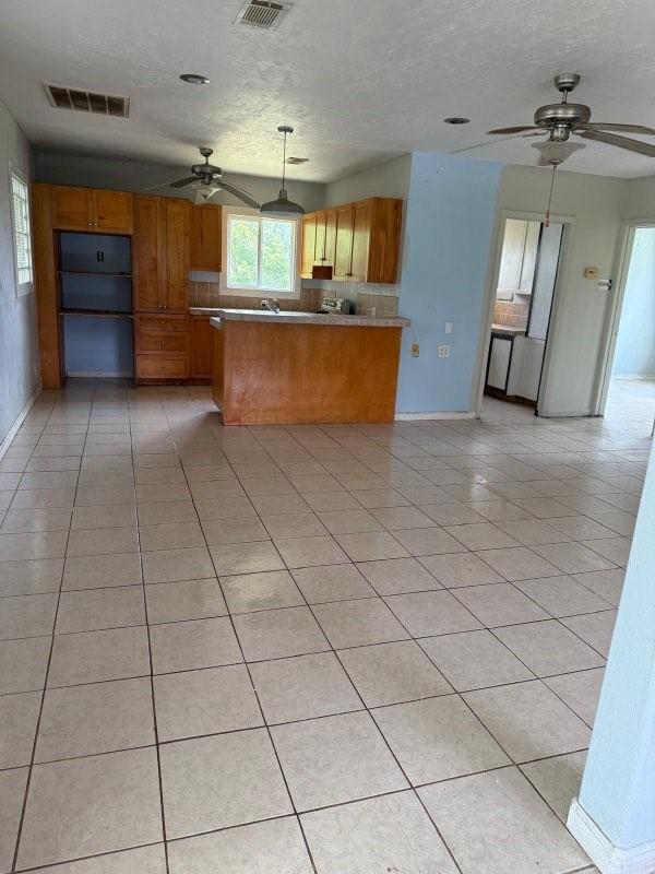 231 Bayshore Rd, Anahuac, TX 77514 - kitchen with ceiling fan, brown cabinetry, a peninsula, light tile patterned floors, and a textured ceiling