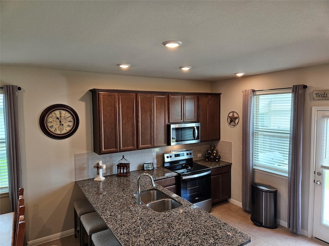 177 Blooming Trl, Kyle, TX 78640 - kitchen with appliances with stainless steel finishes, a sink, backsplash, dark brown cabinetry, and dark stone countertops