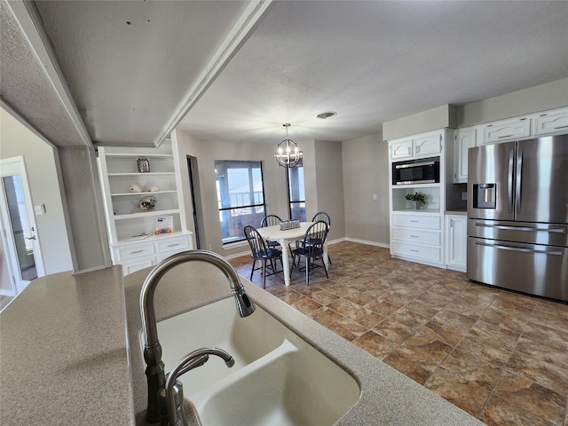 482 W Cattle Dr, Onalaska, TX 77360 - kitchen with appliances with stainless steel finishes, a sink, white cabinets, stone finish flooring, and a chandelier