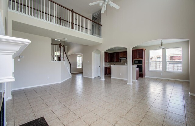 3410 Walden Creek Ln, Pearland, TX 77581 - unfurnished living room featuring ceiling fan, light tile patterned floors, a towering ceiling, arched walkways, and baseboards