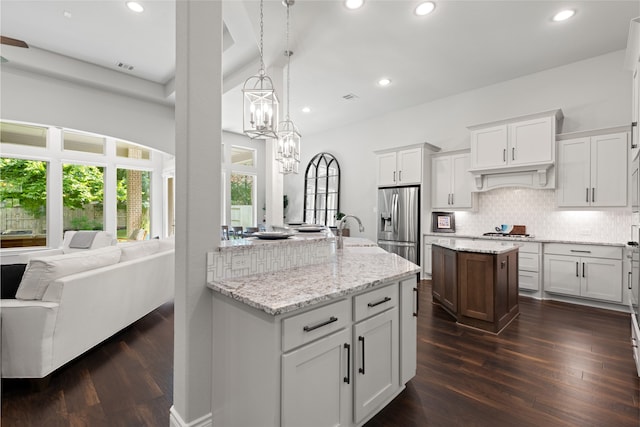 127 Evening Tide Ct, Conroe, TX 77318 - kitchen with stainless steel fridge, an island with sink, decorative backsplash, a chandelier, and dark wood-type flooring