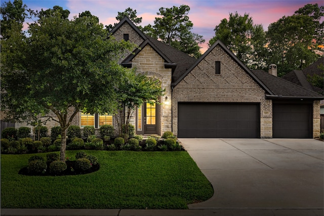 127 Evening Tide Ct, Conroe, TX 77318 - french country home with an attached garage, concrete driveway, a yard, roof with shingles, and brick siding