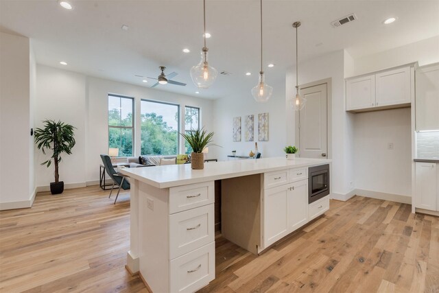 1414 Wichman St, Houston, TX 77007 - kitchen featuring stainless steel microwave, recessed lighting, a kitchen island, light wood-style flooring, and white cabinets