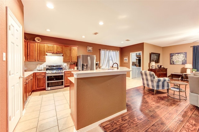 2714 San Marco Ln, League City, TX 77573 - kitchen featuring appliances with stainless steel finishes, under cabinet range hood, light countertops, an island with sink, and brown cabinets