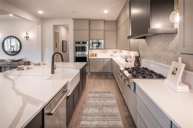 21742 Grayson Highlands Way, Porter Heights, TX 77365 - kitchen featuring appliances with stainless steel finishes, light wood-type flooring, gray cabinetry, a sink, and wall chimney exhaust hood
