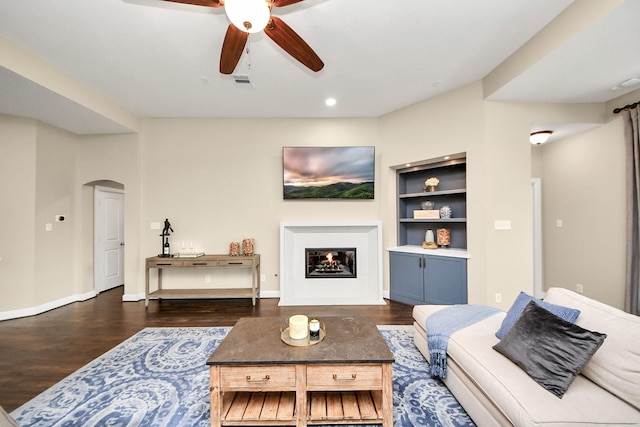 14006 Alex Landing Dr, Humble, TX 77396 - living area featuring arched walkways, dark wood-style flooring, built in shelves, a ceiling fan, and a fireplace with flush hearth