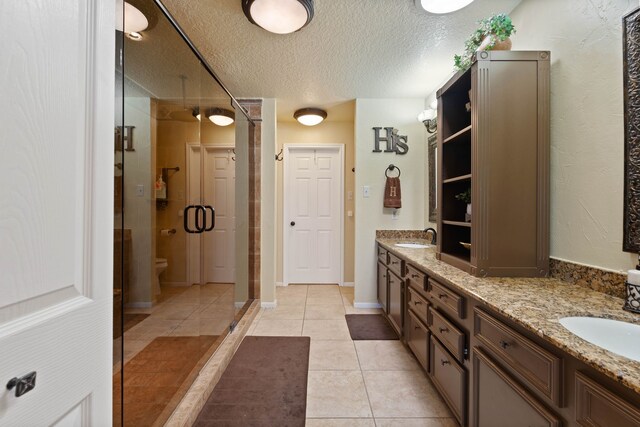 2117 Gunwale Cir, Willis, TX 77318 - bathroom with a textured ceiling, double vanity, a shower stall, tile patterned floors, and toilet